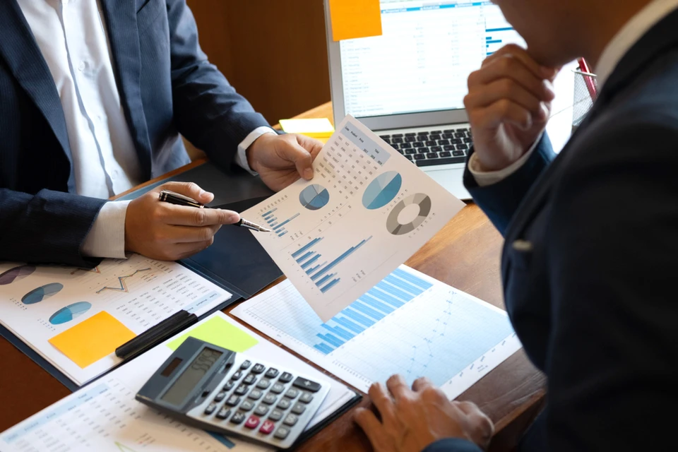 Femme travaillant sur documents financiers dans bureau moderne, utilisant calculatrice et stylo pour analyser des données comptables